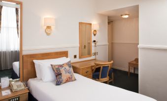 a bed with a white sheet and pillow is in a room with a desk , chair , and mirror at Berjaya Eden Park London Hotel