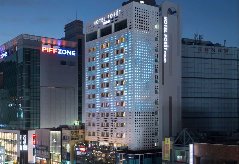 "a tall building with the words "" pifzone "" written on it is surrounded by other buildings at night" at Hotel Foret Premier Nampo