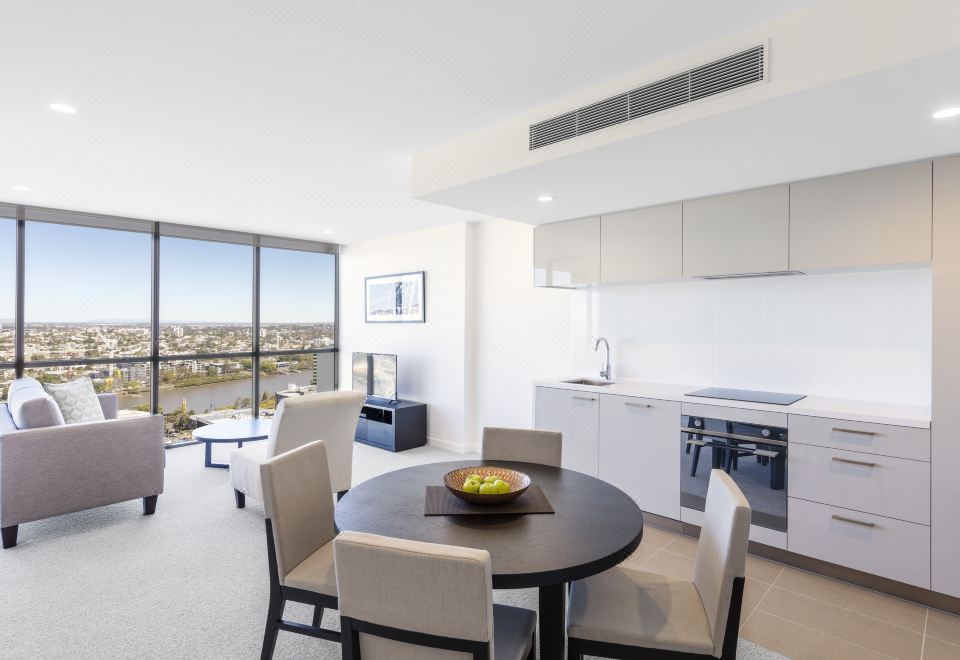 a modern living room and kitchen area with a large window , white furniture , and a green fruit bowl on the table at The Milton Brisbane