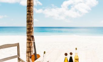 a beach table is set with various food items , drinks , and utensils , offering a serene and peaceful view of the ocean at North Island, a Luxury Collection Resort, Seychelles