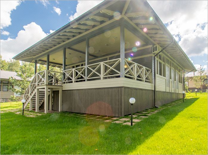a large wooden house with a balcony and green grass , under a sunny sky with clouds at Palisad