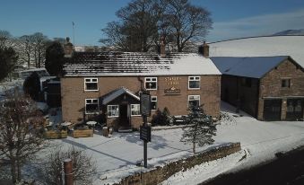 a brick building with a snow - covered roof , situated in a snowy city street surrounded by trees at The Stanley Arms