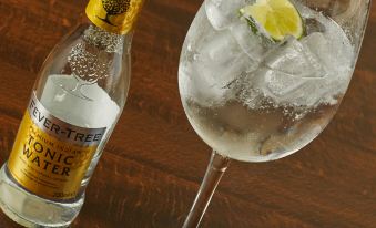 a bottle of tonic water on a wooden table , accompanied by a glass filled with ice and a slice of lemon at The Cadogan Arms