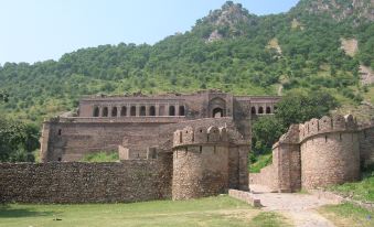 a stone wall with a few windows is in front of a grassy area and a mountain at Pinky Hotel