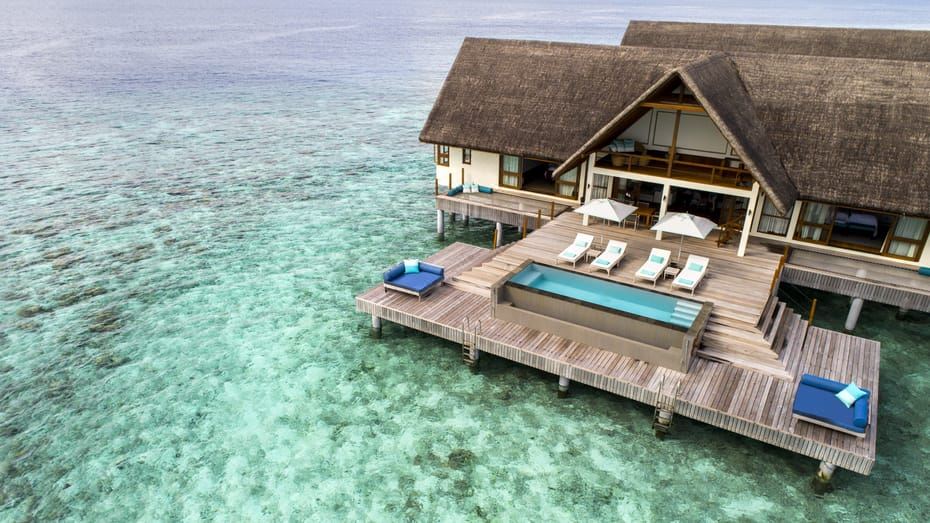 an aerial view of a wooden deck overlooking the ocean , with a swimming pool and lounge chairs nearby at Four Seasons Resort Maldives at Landaa Giraavaru