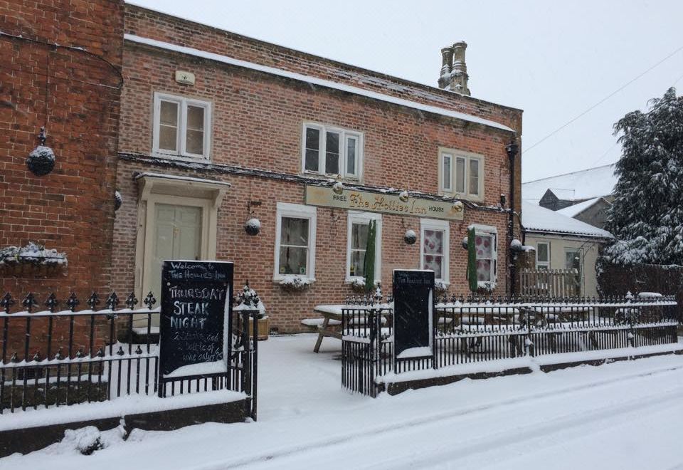 a brick building with a large sign on the side , surrounded by snow - covered ground and trees at The Hollies Inn