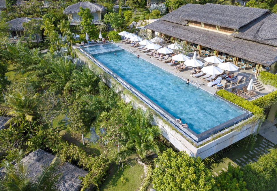 a large outdoor swimming pool surrounded by trees , with several lounge chairs and umbrellas placed around it at Lahana Resort Phu Quoc & Spa