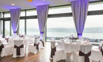 a room with purple curtains and white tablecloths has several round tables set up for an event at Belvoir Swiss Quality Hotel