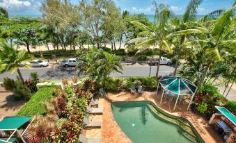 a tropical resort with a swimming pool , lush greenery , and a beach in the background at On the Beach Apartments