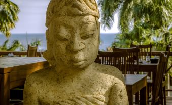a stone statue of a woman sitting on a wooden bench in front of a body of water at Janji Laut Resort