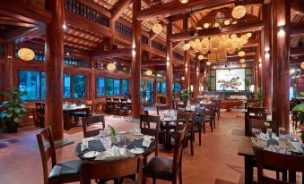 a large wooden restaurant with multiple dining tables , chairs , and a tv screen on the wall at Tam Coc La Montagne Resort & Spa