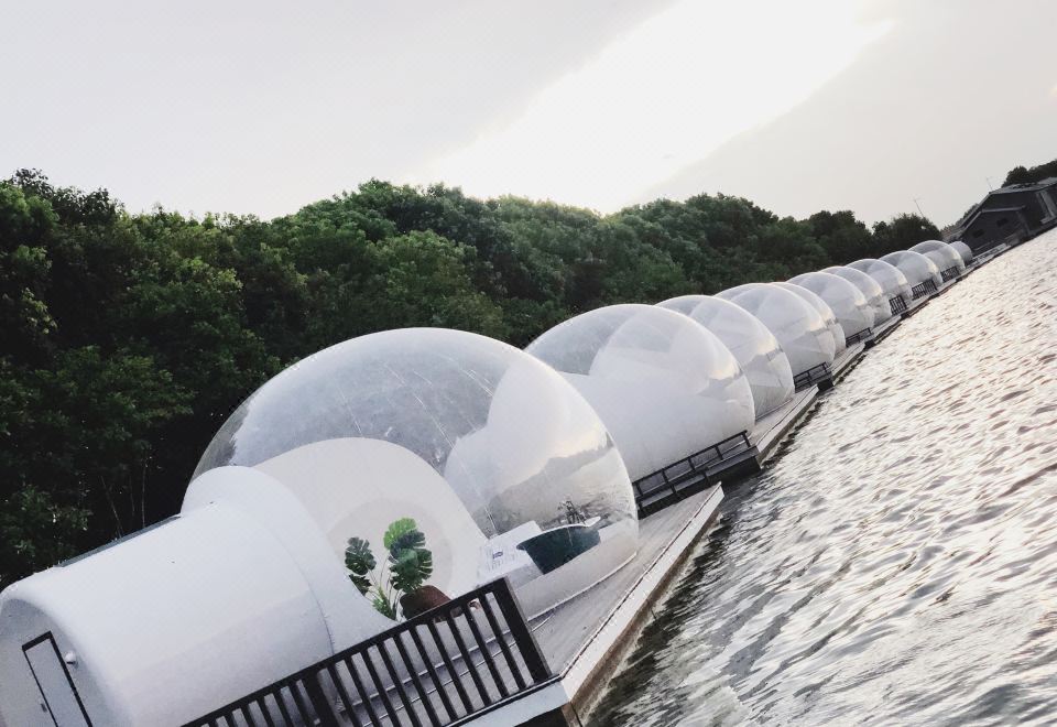 a row of white domed structures on the edge of a body of water , with trees in the background at Lucen