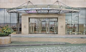 The entrance to a large building features glass doors and a stone walkway leading up to it at Rambler Oasis Hotel