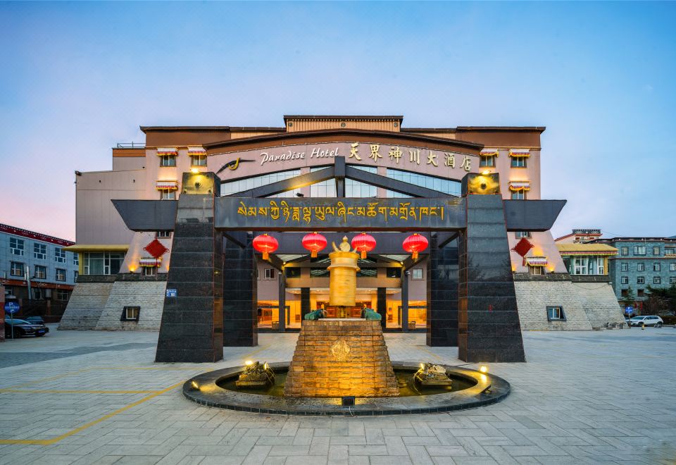 a large building with a fountain in front of it , surrounded by grass and trees at Paradise Hotel