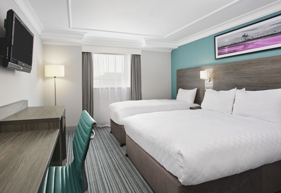 a modern hotel room with two beds , a desk , and a window , all neatly arranged at Leonardo Hotel Middlesbrough - Formerly Jurys Inn