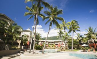 a resort with a large pool surrounded by palm trees , and several buildings in the background at Mantra Amphora