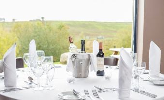 a table is set with wine glasses , a bottle of wine , and various utensils , overlooking a field at The Twice Brewed Inn