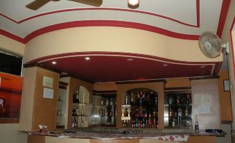 a bar with a red and white ceiling , a ceiling fan , and various bottles and wine glasses at Pinky Hotel