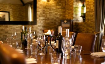 a dining table is set with wine glasses , bottles of wine , and candles in a dimly lit room at The Woolpack Inn