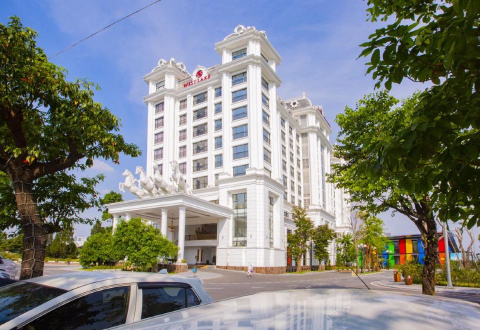 a white hotel building with a large sculpture on top and cars parked in front at Westlake Hotel & Resort Vinh Phuc