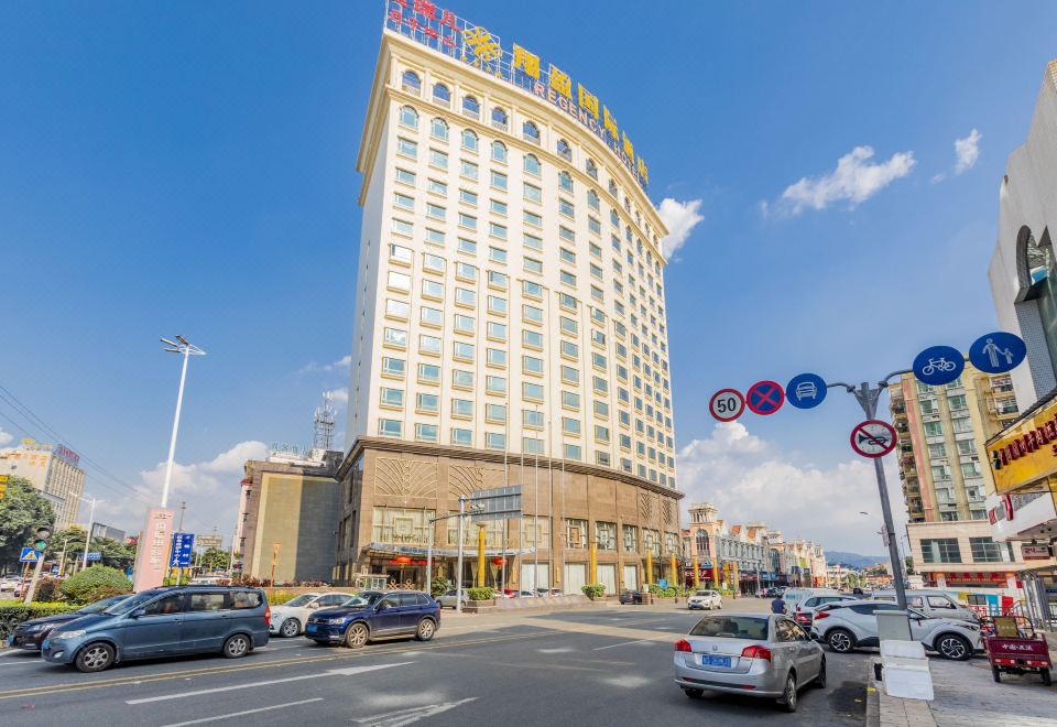 a tall hotel building surrounded by a parking lot , with numerous cars parked in front of it at Regency Hotel