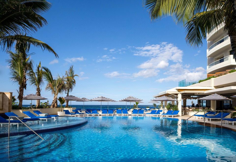 a large outdoor swimming pool surrounded by palm trees , with several lounge chairs and umbrellas placed around the pool area at Condado Vanderbilt Hotel