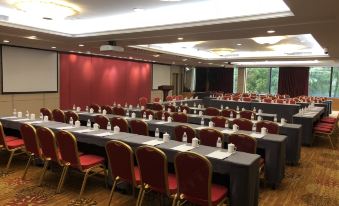 A spacious event room is arranged with long tables and red chairs facing the front at City Hotel