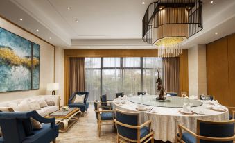 a modern living room with a large window , blue couches , and a dining table set for a meal at Sanya Xizang Hotel