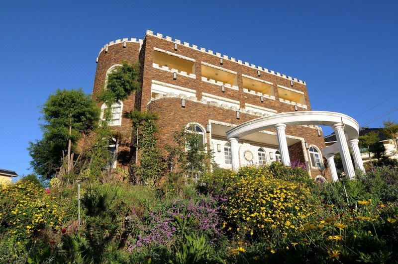 a large brick building with a white roof and columns is surrounded by greenery and flowers at Huis Ten Bosch