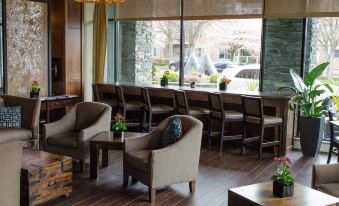 a cozy coffee shop with wooden tables , chairs , and a view of a parking lot outside the window at Oswego Hotel
