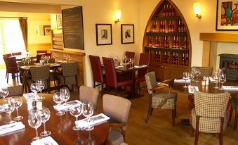 a restaurant with wooden tables and chairs , wine glasses , and wine bottles on display in the background at The Cadogan Arms