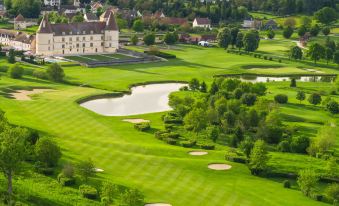 an aerial view of a golf course with green grass , a pond , and a building in the background at Hotel Golf Chateau de Chailly
