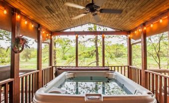 a hot tub is surrounded by a wooden deck and ceiling , with a view of trees in the background at New Hochatown Lodge