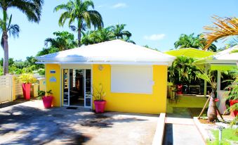 a small yellow building with a white roof and a sign on the side , surrounded by palm trees at Majesty Palm Hôtel