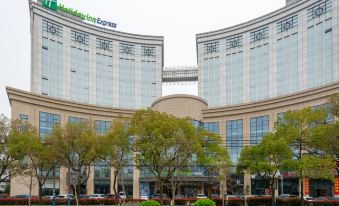 a large , modern building with a green logo on the side is surrounded by trees at Holiday Inn Express