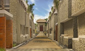 a long , narrow alleyway with a stone building on the left side and palm trees on the right side at Merusaka Nusa Dua