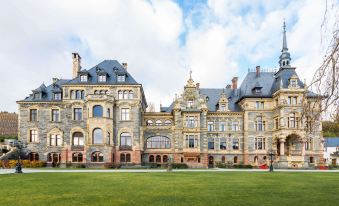 a grand , multi - story building with stone walls and red brick accents , surrounded by green lawns and trees at Schloss Lieser, Autograph Collection