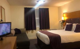 a well - lit hotel room with a bed , curtains , and a tv , along with a black couch at Purple Roomz Preston South