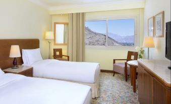 a hotel room with two beds , a window offering a view of mountains , and armchairs at Steigenberger Hotel & Nelson Village, Taba