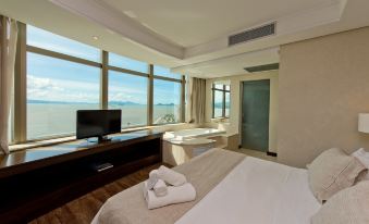 a hotel room with a large window overlooking the ocean , a bed with towels on it , and a television at Majestic Palace Hotel