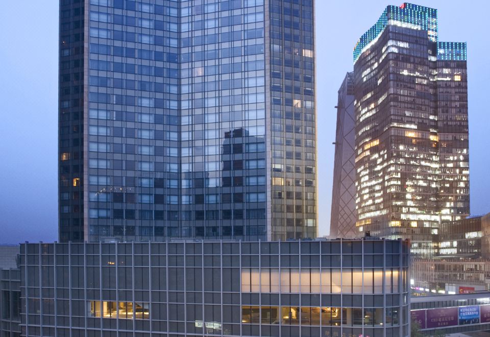 A large building with numerous windows is visible at dusk in the city, as observed from a distance at Grand Millennium Beijing