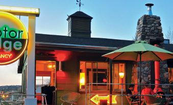 a rooftop patio with umbrellas , chairs , and tables , as well as a clock tower in the background at Motel Lodge