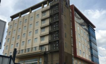 a large , modern building with multiple floors and balconies , surrounded by a metal fence and under a cloudy sky at Sapphire Sky Hotel & Conference