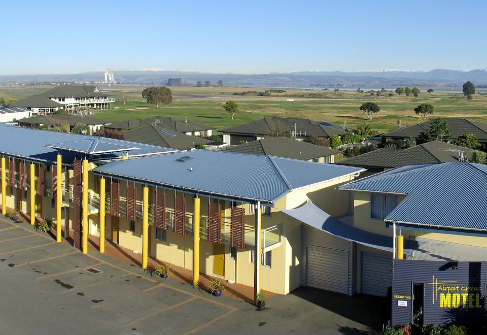 a modern building with a blue roof , surrounded by grass and trees , under a clear blue sky at Greens Motel