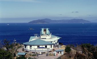 a large building with a blue roof is situated on the edge of a cliff overlooking the ocean at Daiwa Roynet Hotel Oita