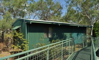 a green building with a balcony and a railing , surrounded by trees and bushes , under a clear blue sky at Parry Creek Farm Tourist Resort & Caravan Park