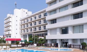 a large swimming pool is located in front of a white hotel with balconies and trees at OARAI HOTEL