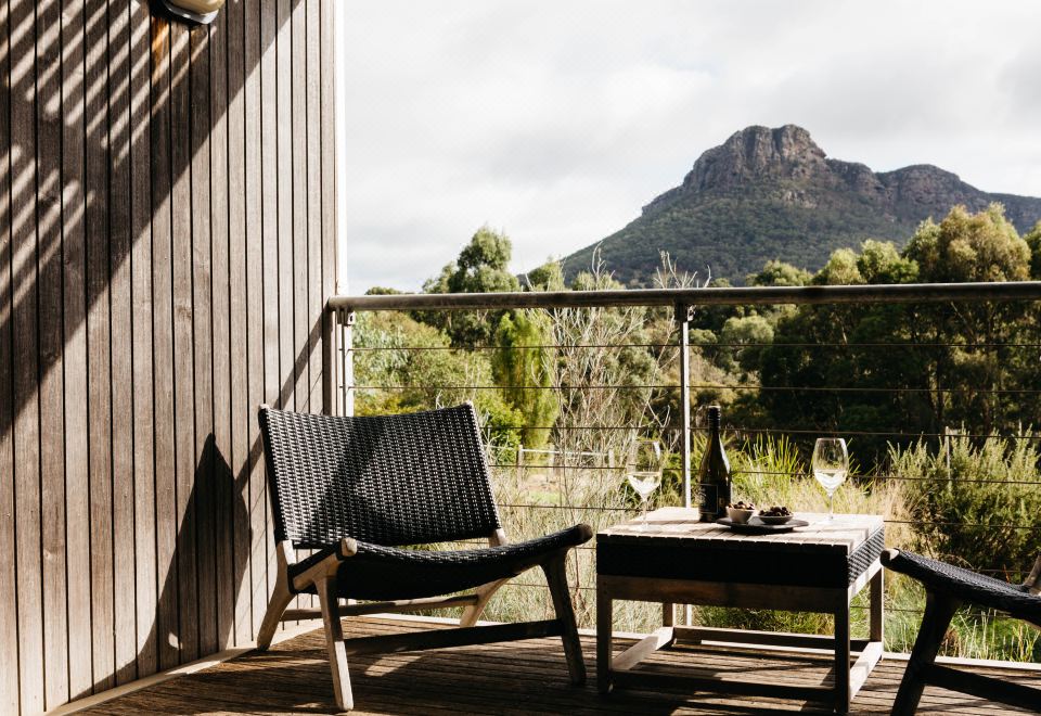 a wooden balcony overlooking a mountain , with a chair and wine glass placed on the deck at Royal Mail Hotel