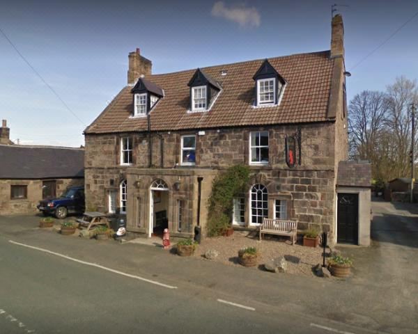 a large stone building with a black roof , located on the side of a road at Red Lion Inn