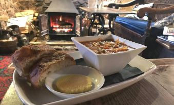 a plate of food with a bowl of sauce and a slice of bread is placed on a table near a fireplace at The Nobody Inn